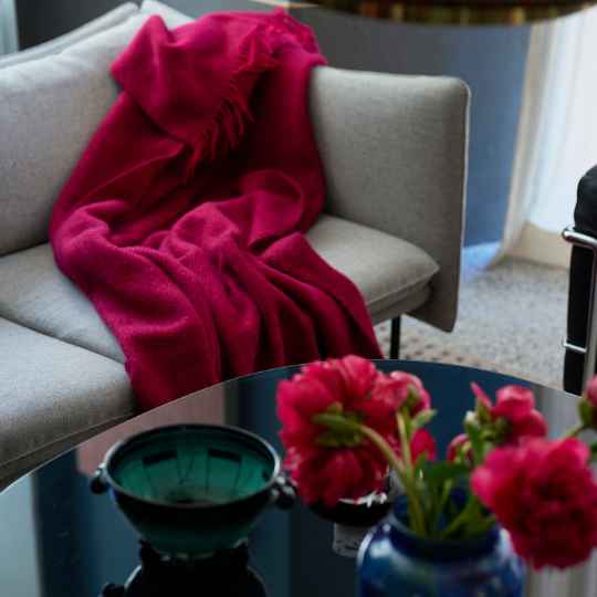 Red blanket draped over a gray chair with a table featuring a teapot and flowers in a room.