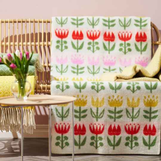 tulip wool blaket on a bench with a pile of throws and table with a vase of flowers