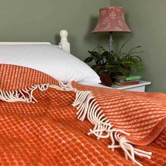 velvet rust lambswool throw on a bed with a green back ground and lamp