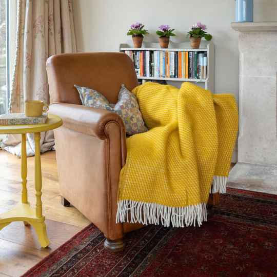 yellow lambswool throw in a brown chair with a side table and bookcase in the background