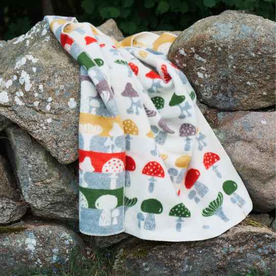 lambswool blanket with a colourful repeat mushroom pattern on rocks