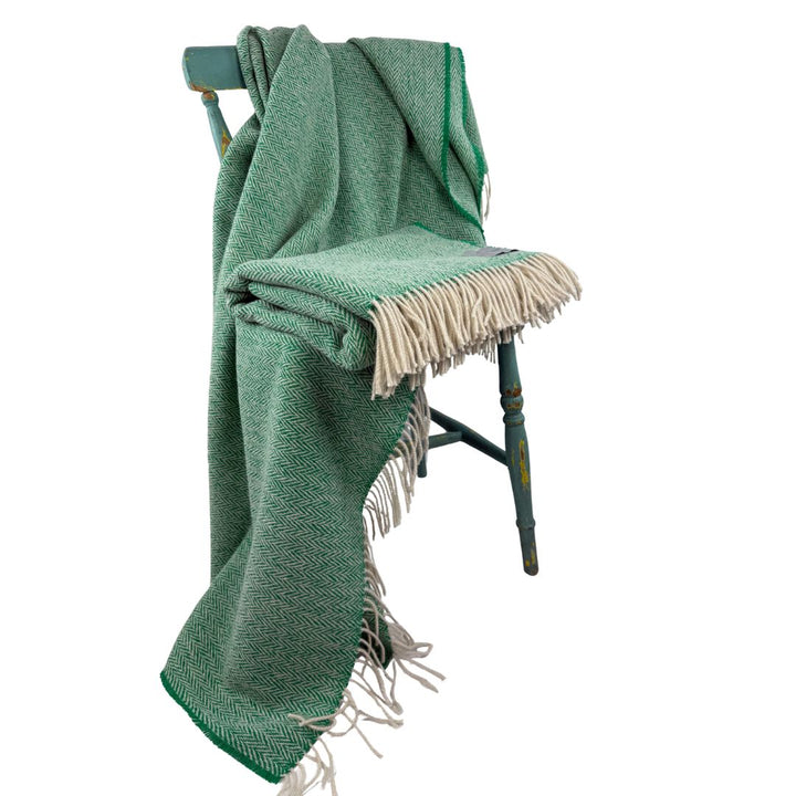 Green blanket with fringes draped over a wooden chair on a white background