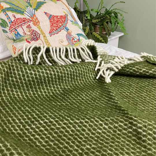 velvet avocado wool throw on a bed with cushions and plant in the background