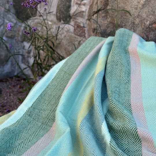 birka meadow lambswool throw showing a striped pattern agianst a stone wall