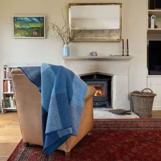Blue block check wool throw on an armchair in front of a lit log burner
