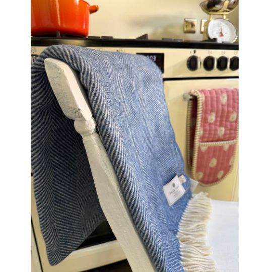 A blue and white herringbone patterned throw blanket with fringe, draped over a white chair in a cozy kitchen setting.
