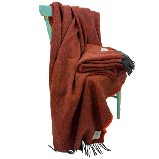 burnt ornage wool throw draped over a chair with grey tassles on a white background