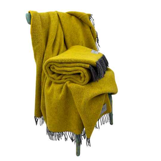 buttercup yellow blanket with fringes on a chair against a white background