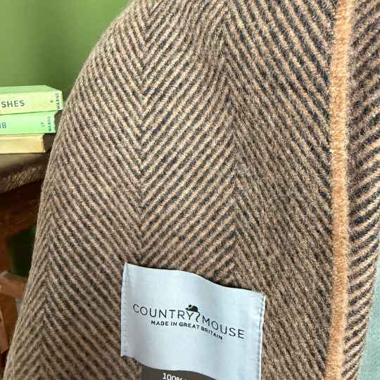 Herringbone patterned  brown wool throw with a 'Country Mouse' label on a blurred background