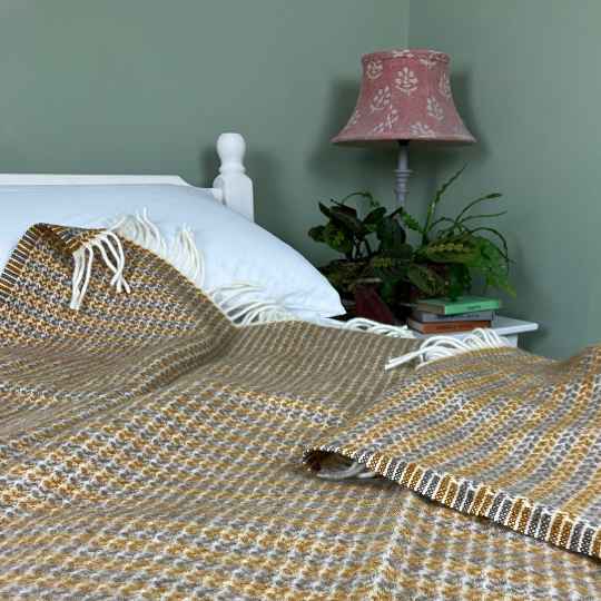 Bed with a patterned blanket, white pillow, and nightstand with lamp and books against a green wall.