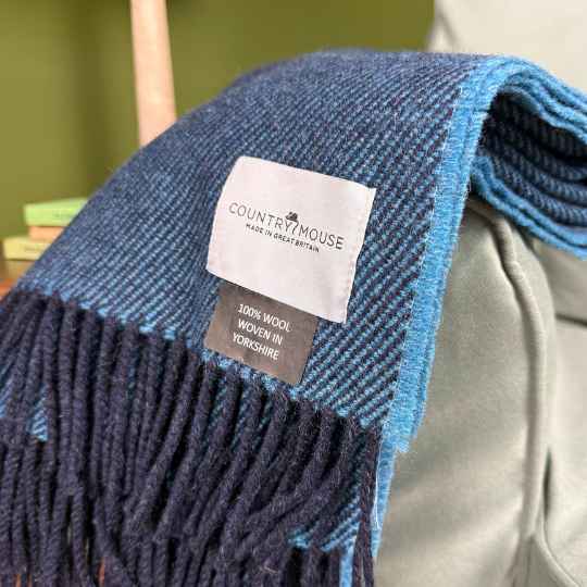 Blue and black checkered blanket with a 'Country Mouse' label on a gray surface.