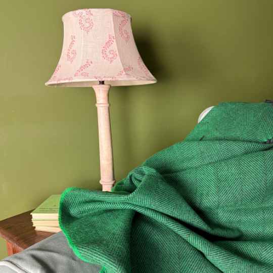 Lamp with pink floral shade on a wooden stand against a green wall. with a green blanket