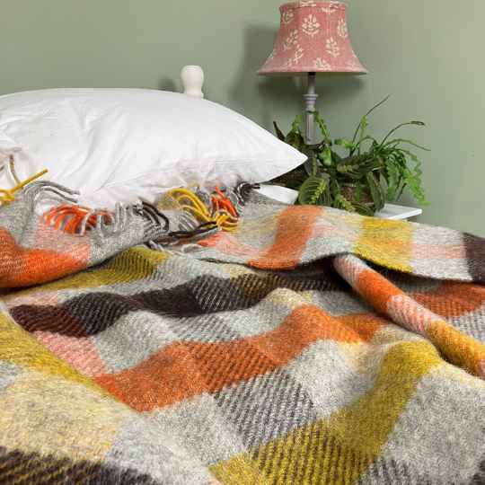 gotland multi yellow wool blanket on a bed with a lamp and plant in the background