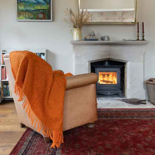 Gotland orange wool throw on a armchair next to a lit wood burner
