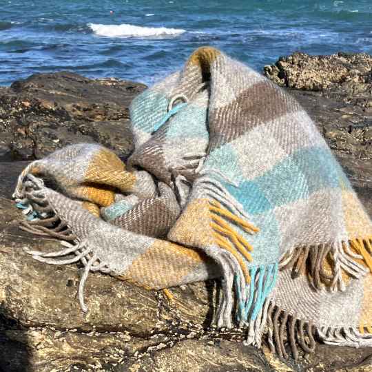 Gotland turquoise Plaid  throw blanket with fringes on a rock by the ocean