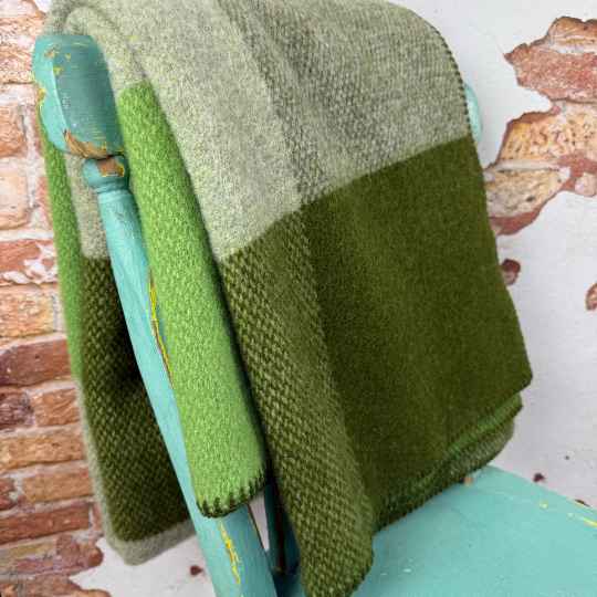 Green woven blanket draped over a teal chair against a brick wall.