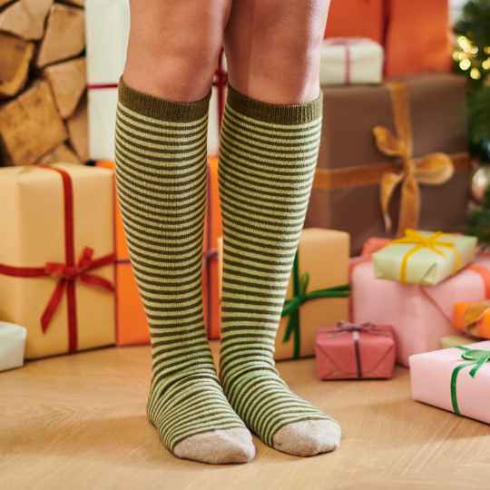 Green and white striped knee-high socks worn by a person in front of Christmas presents.