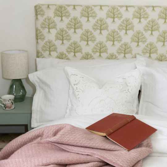 Harald dusty pink on a bed with a book. White bed linen and a green bedside table