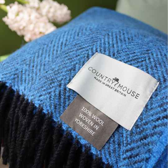 Blue and black woven blanket with a 'Country Mouse' label on a blurred background