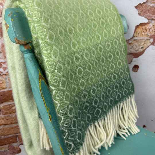 Green textured wool blanket draped over a teal chair with a brick wall background