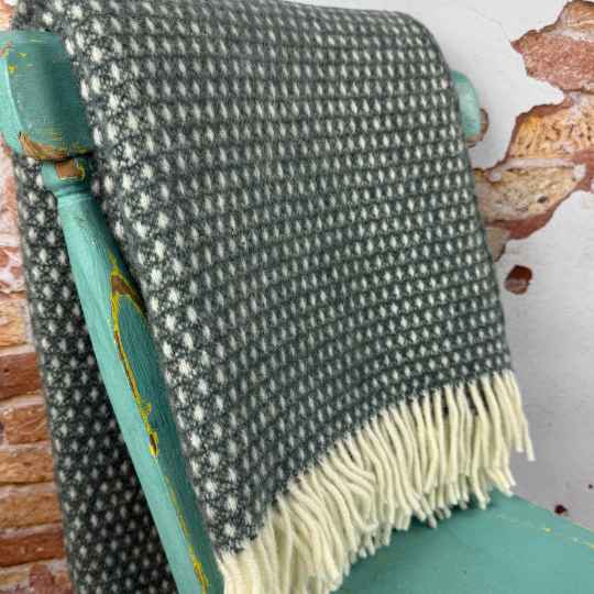 Textured green and white blanket draped over a teal chair with a rustic background.