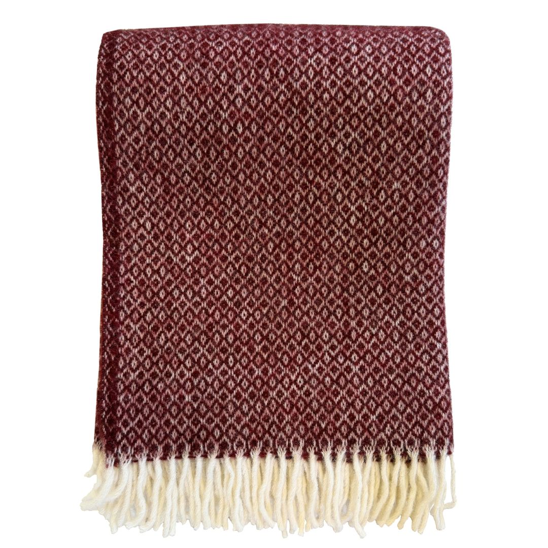 A folded woven throw blanket in a deep burgundy red with a repeating cream diamond pattern and cream fringe along the bottom edge, shown against a plain white background.