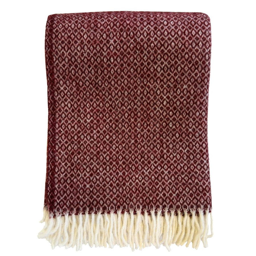 A folded woven throw blanket in a deep burgundy red with a repeating cream diamond pattern and cream fringe along the bottom edge, shown against a plain white background.