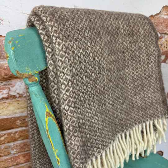 Brown woven wool and alpaca blanket draped over a teal chair with a brick wall background