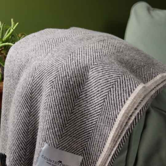 millstone grey herringbone throw on a chiat with a plant in the background