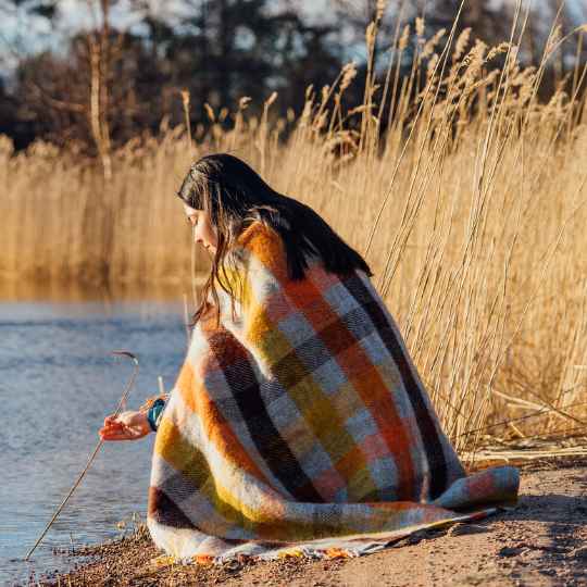 person wrapped in gotland multi yellow wool throw by a lake