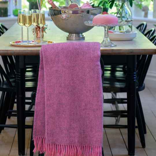 Pink throw blanket draped over a chair with a dining table and chairs in the background.