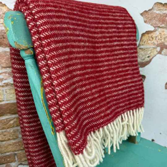 Red woven blanket with white fringe draped over a green chair against a textured wall.