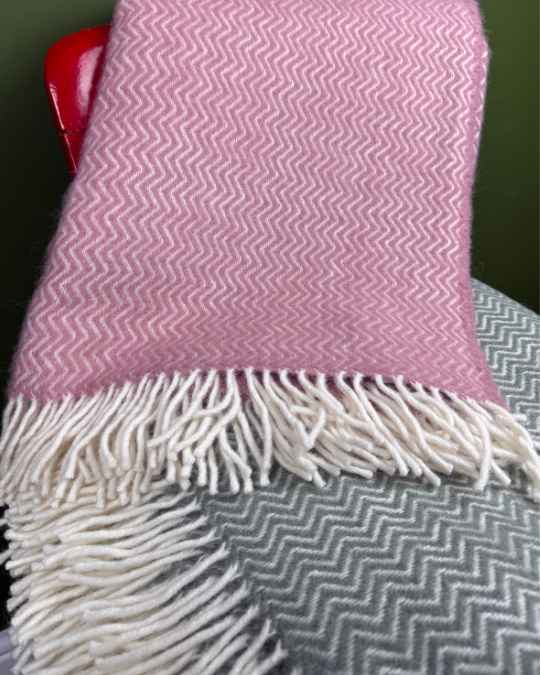 Pink and green chevron-patterned blanket with white fringe draped over a chair.