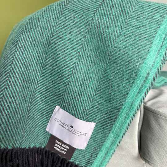 Green herringbone blanket with a visible label on a soft focus background