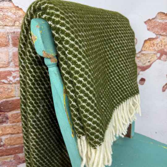 Green and white patterned throw blanket draped over a teal chair against a brick wall.