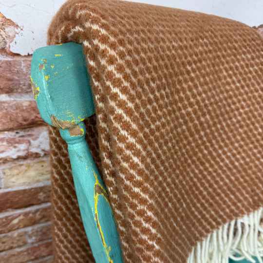 Close-up of a textured brown blanket draped over a turquoise chair with peeling paint.