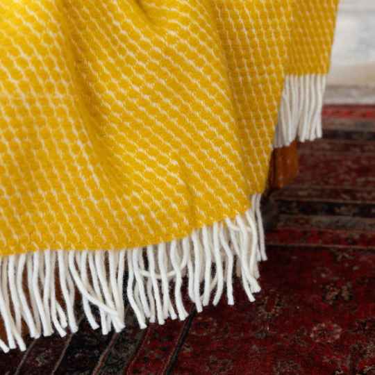 Velvet saffron wool throw close up on an armchair above a red floor rug