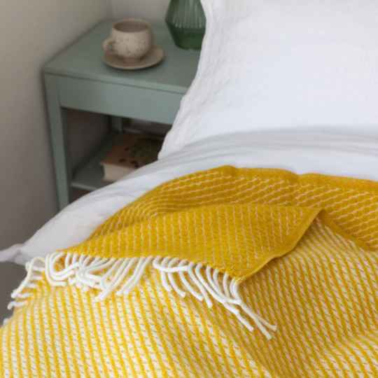 Velvet saffron wool throw on a bed with a green bedside table and white bed linen.