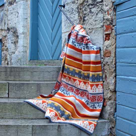 Visby Ochre Colorful patterned blanket draped over stone steps with a blue door in the background