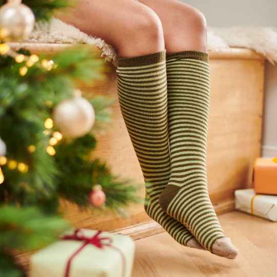 Person wearing striped knee-high socks in front of a decorated Christmas tree with presents.