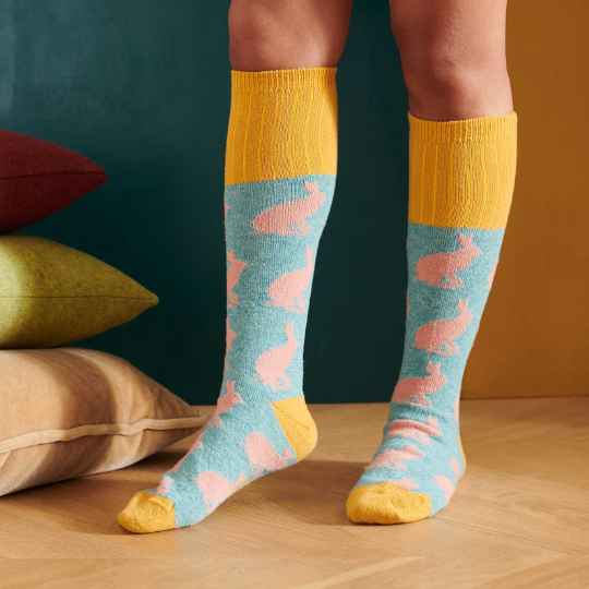 Person wearing colorful socks with a pattern of pink rabbits on a wooden floor.