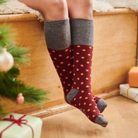 Person wearing red polka dot socks with gray cuffs and toes, sitting by a Christmas tree and presents.