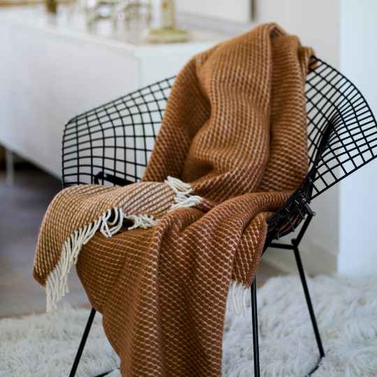brown mocha mousse lambswool throw draped over a black wire chair